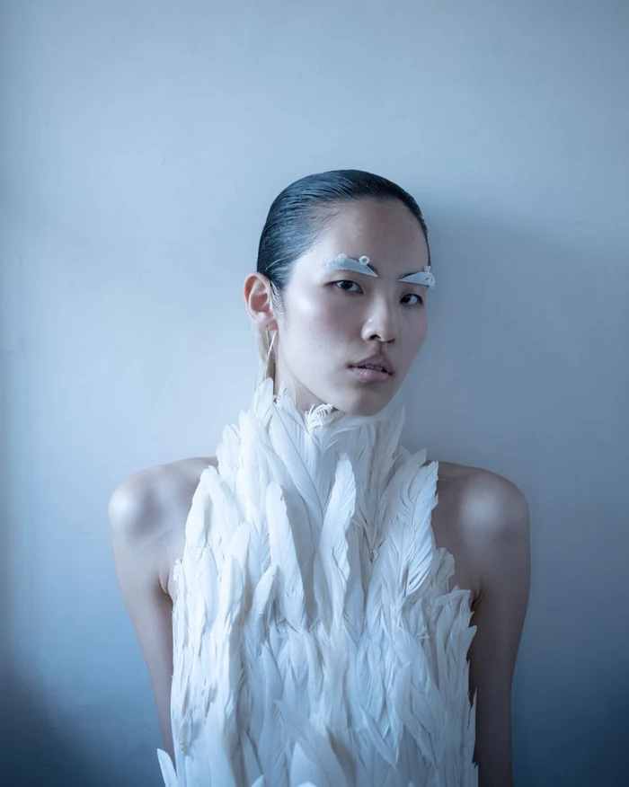 Model Song Ah Woo wearing a white feather collar and avant-garde eyebrow adornments for Exhibition Magazine