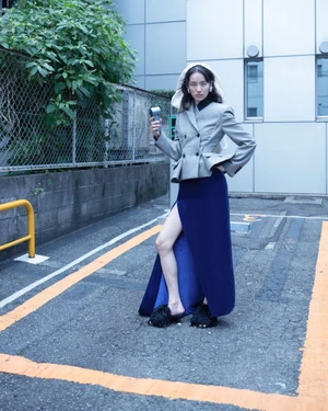 Model Song Ah Woo wearing a grey blazer and blue skirt in an outdoor parking area for Exhibition Magazine.