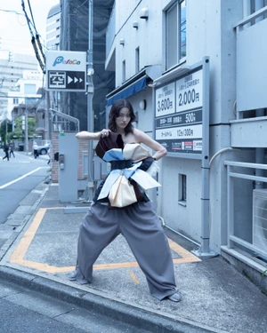 Model Song Ah Woo wearing voluminous grey trousers and an avant-garde structured top standing on an urban street
