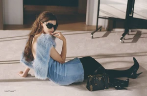 Model in blue fur top and sunglasses reclining on a carpeted floor with a black handbag