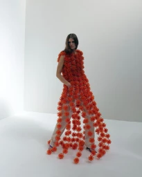 Model wearing a textured orange floral tunic over trousers against a plain white studio backdrop.