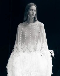 Model in white sheer cape with lace detailing and feathered hem for Balenciaga SS27 BOH photographed by Fran Gomez de Villaboa.