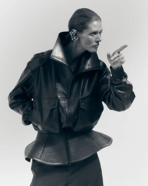 Model in black leather jacket pointing forward against a white seamless background for WWD