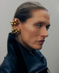 Model wearing a large gold cluster ear cuff and a black leather jacket against a neutral studio background