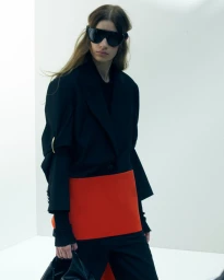 Model wearing dark sunglasses, black jacket, and bright red skirt panel against a clean white studio background.