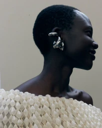 Profile portrait of a Black model wearing a large silver ear cuff and a textured white garment for Balenciaga SS27.