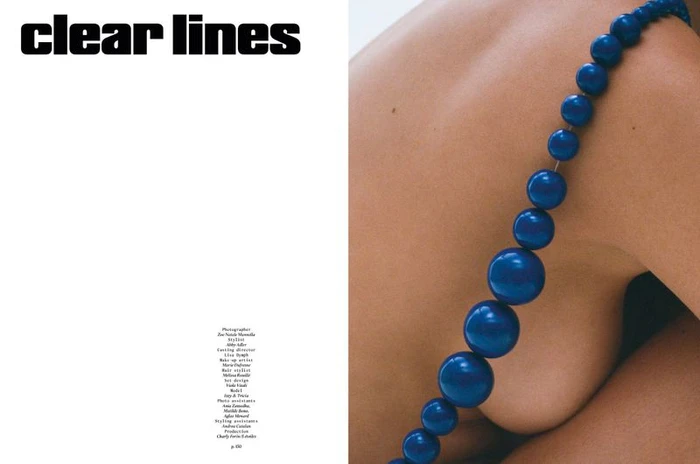 Close-up portrait of a person's shoulder draped with a striking strand of large blue beads against a clean white background