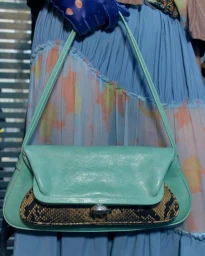 Mint green leather shoulder bag with snakeskin front panel detail held against a blue pleated skirt.