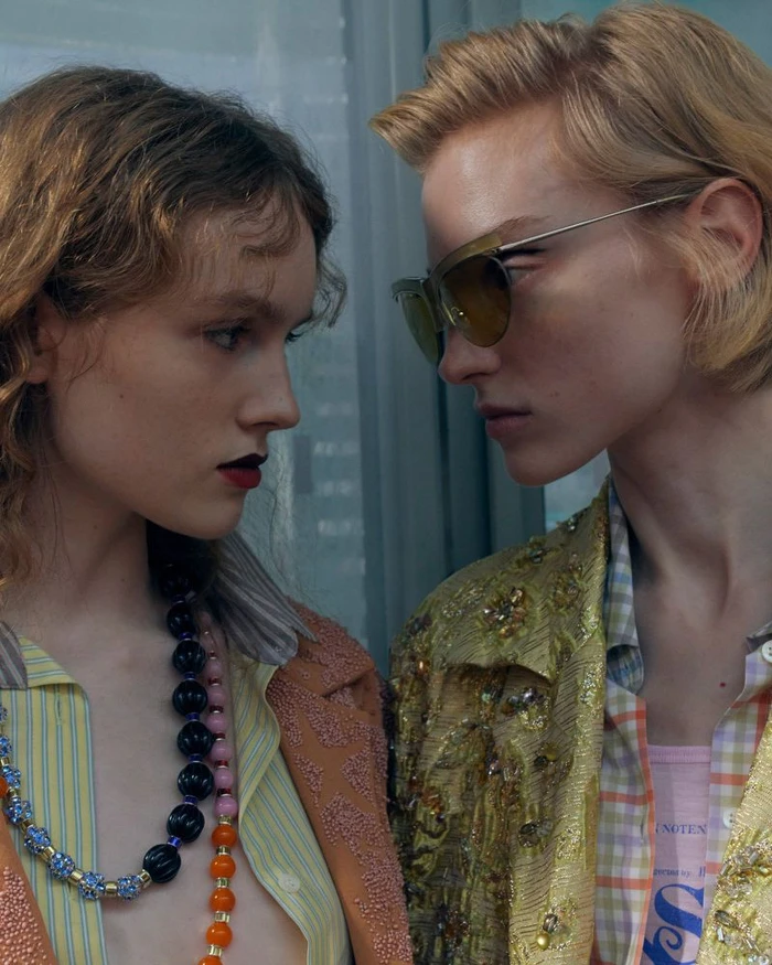 Two female models facing each other closely wearing layered patterned clothing and statement bead necklaces