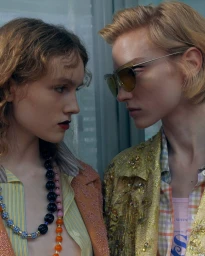 Two female models facing each other closely wearing layered patterned clothing and statement bead necklaces