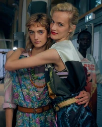 Two smiling models embracing backstage at the Dries Van Noten fashion show, wearing patterned garments and belts