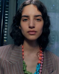 Close-up portrait of a model wearing a striped blazer and beaded necklaces by Julian Klausner for WWD