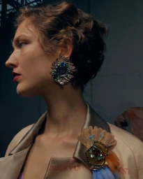 Profile portrait of a model with short dark hair wearing ornate statement earrings and a decorated satin jacket by WWD