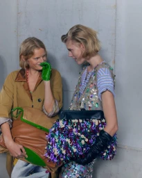 Two models backstage at Dries Van Noten wearing designer apparel and holding large statement handbags
