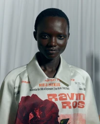 Model with short dark hair wearing a white printed collared shirt against a white curtain background