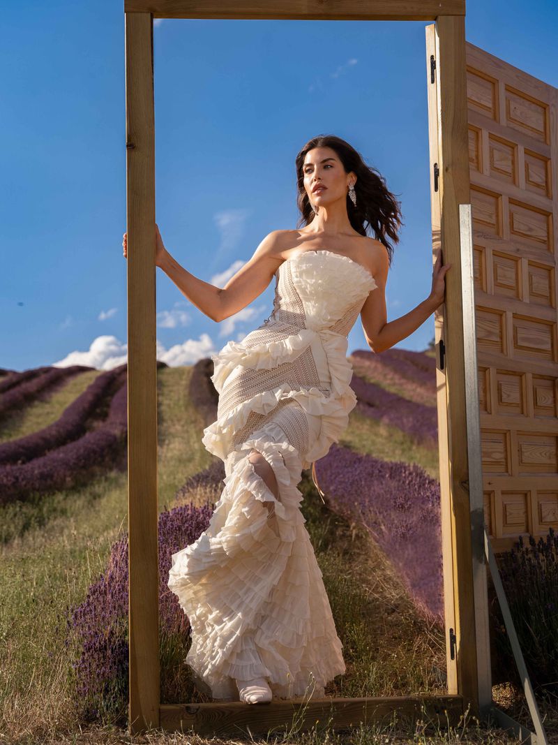Woman in a white dress posing in a lavender field, framed by a wooden doorway under a blue sky. Fashion and outdoor photography.