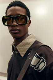 Model wearing dark sunglasses, striped shirt, and brown sweater against a neutral background for Burberry SS27 BOH.