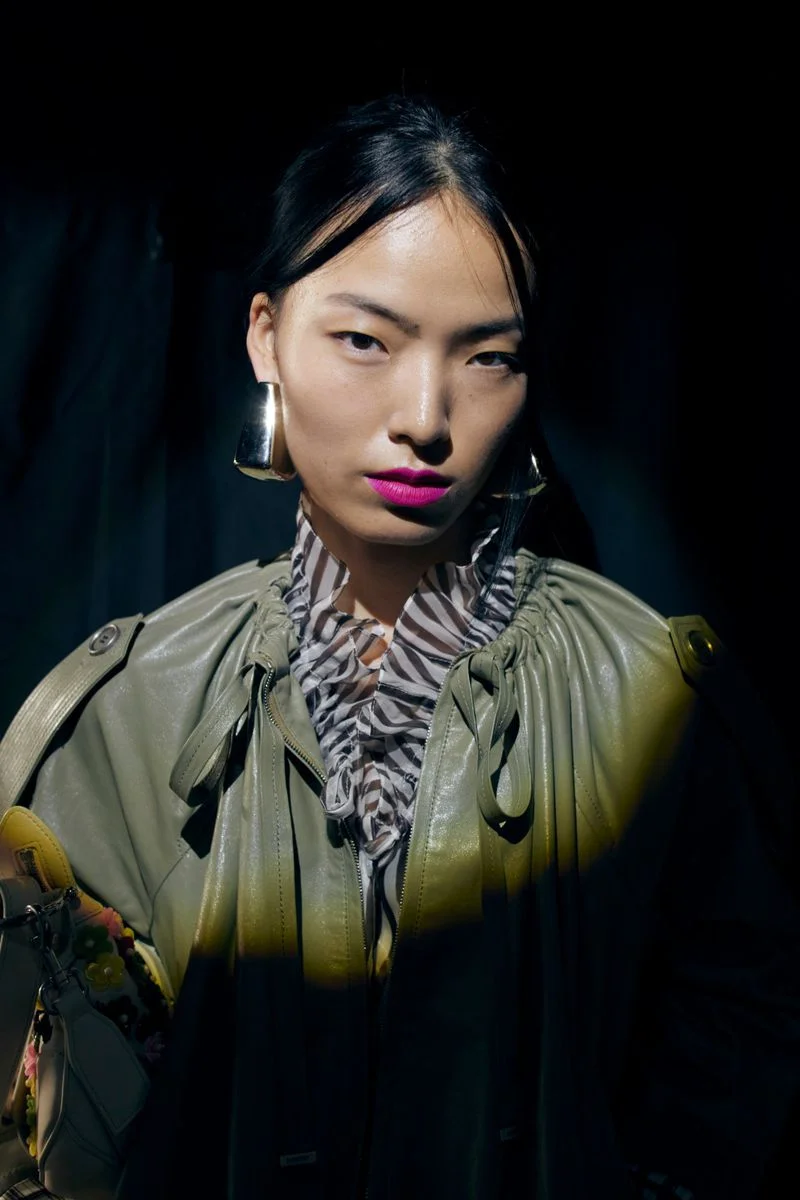 Model with dark hair wearing an olive green coat and statement earrings for Burberry SS27