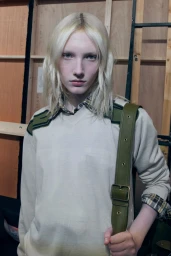 Model with blonde hair wearing cream sweater and plaid shirt backstage at Burberry SS27