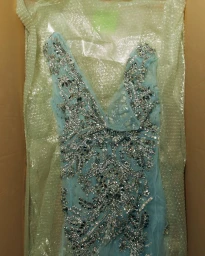 Light blue sleeveless evening dress heavily embellished with silver crystals lying inside a cardboard shipping box lined with bubble wrap.