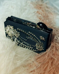 Black embellished clutch bag resting on soft white and peach ostrich feathers for Erdem SS27 BOH