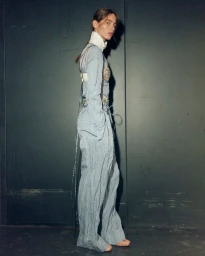 Model standing sideways in a matching light blue textured top and trousers against a dark panel background