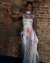 Model in a pale blue floral print gown posing against an exposed brick wall for WWD Erdem SS27 BOH