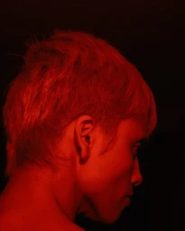 Profile view of a person with short hair bathed in dramatic red light against a dark background