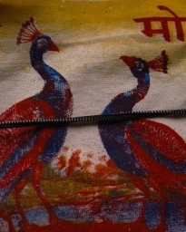 Textile print featuring two peacocks facing each other with red and blue coloring, crossed by a thin dark wire.