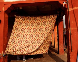 Patterned fabric hanging between red pillars in an architectural alcove with feet visible underneath