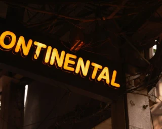 Illuminated yellow neon sign reading CONTINENTAL against a dark outdoor urban background with entangled wires