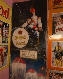 Large poster of a man in traditional Indian marching band uniform seated beside a bass drum with Royal Band text