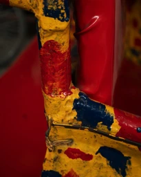 Close-up of a brightly painted yellow, red, and blue textured metal frame with a red shiny fabric background.