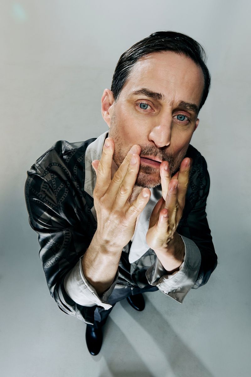 Actor Clemens Schick looking upward with hands near his face for Sleek Magazine, photographed by Szymon Stępniak.