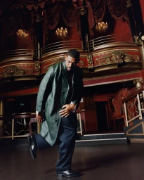 Aaron Pierre wearing a dark green leather coat and dark trousers inside an ornate theatre for Esquire UK