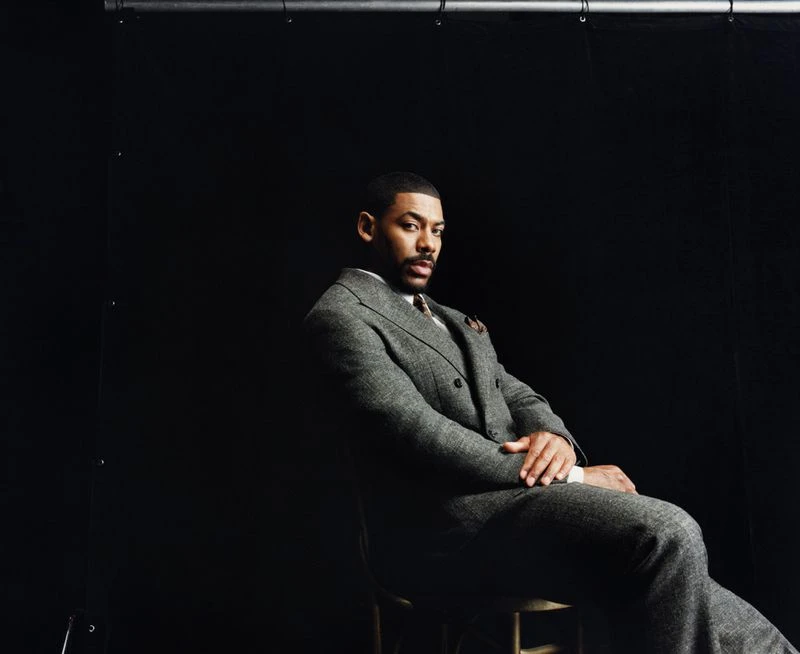 Actor Aaron Pierre seated in a grey tweed suit against a dark background for Esquire UK photographed by Olivia Lifungula.