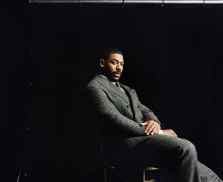 Actor Aaron Pierre seated in a grey tweed suit against a dark background for Esquire UK photographed by Olivia Lifungula.