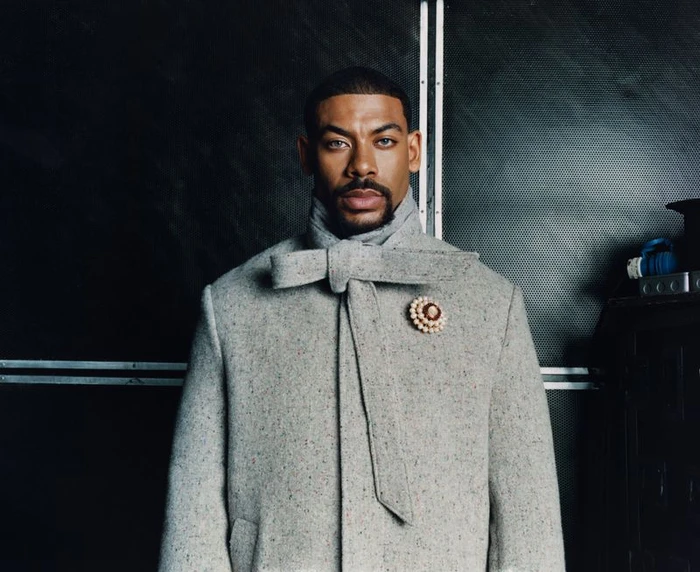 Portrait of actor Aaron Pierre wearing a grey tweed coat with a bow tie and brooch for Esquire UK