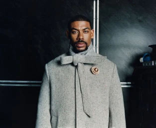Portrait of actor Aaron Pierre wearing a grey tweed coat with a bow tie and brooch for Esquire UK