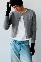 Model wearing a grey cardigan, white t-shirt, blue jeans, and black beanie against a white wall.