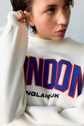 Close-up portrait of a model wearing an off-white crewneck sweatshirt with bold red and blue embroidered lettering.