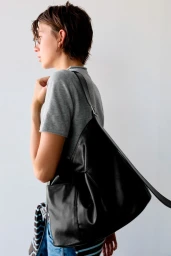 Model wearing a grey t-shirt and carrying a large black leather shoulder bag against a plain white background