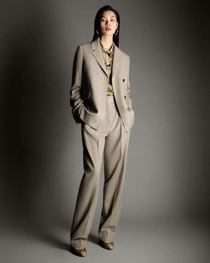 Model Bingbing Liu in a beige trouser suit and silk blouse standing against a grey studio backdrop