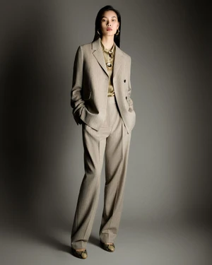 Model Bingbing Liu in a beige trouser suit and silk blouse standing against a grey studio backdrop