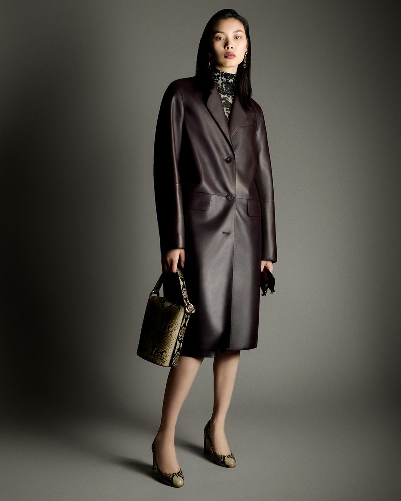 Model Bingbing Liu wearing a dark leather coat and holding a patterned handbag against a grey backdrop