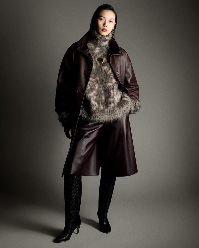 Model Bingbing Liu wearing a burgundy leather coat over a fuzzy turtleneck and tall black boots against a grey seamless backdrop