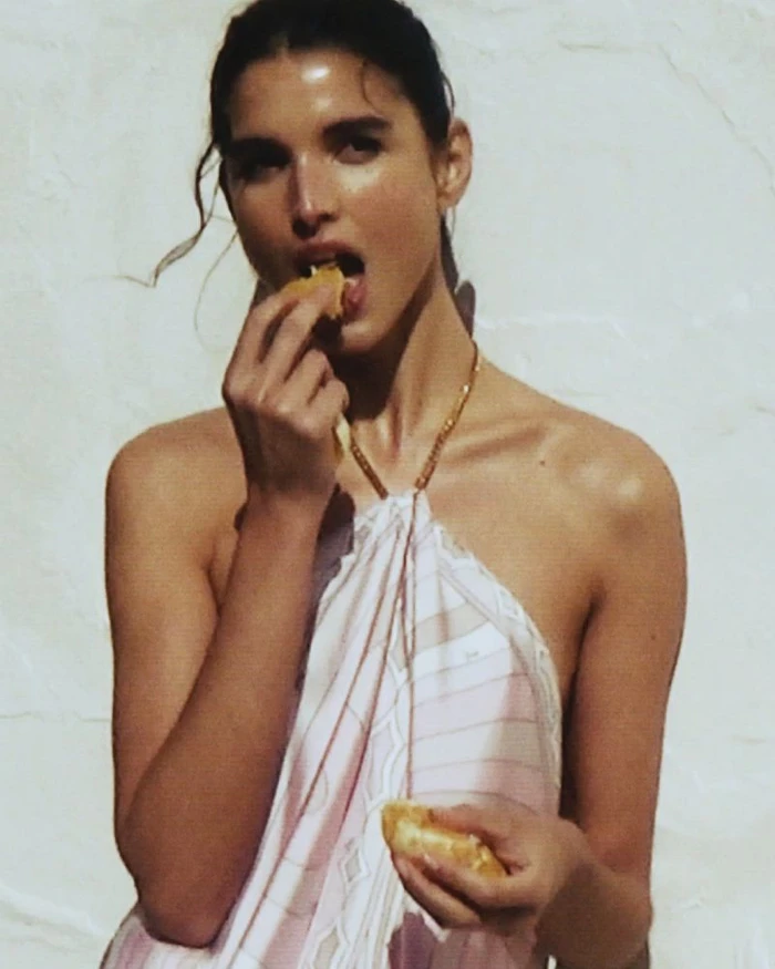 Model in a patterned pink halter top eating pastry against a light textured background for Pucci mytheresa
