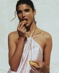 Model in a patterned pink halter top eating pastry against a light textured background for Pucci mytheresa