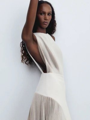 Model in pleated white dress posing against a plain grey backdrop for Alaïa