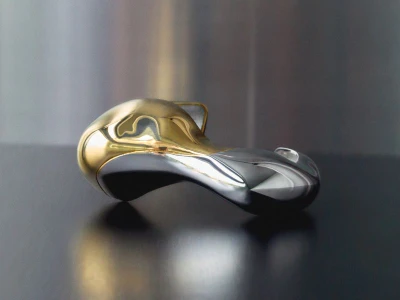 A sculptural metallic object with gold and silver finishes resting on a dark surface against a brushed metal wall.